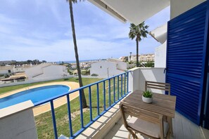 Un balcón con piscina, una mesa con una planta y vistas al mar y edificios.