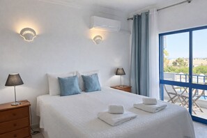 Une chambre à coucher avec un lit, deux lampes de chevet, une fenêtre avec des rideaux et un balcon avec des chaises.