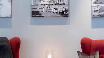 Una habitación con dos sillones rojos, una pequeña mesa de madera con una vela, y tres fotografías enmarcadas en la pared.