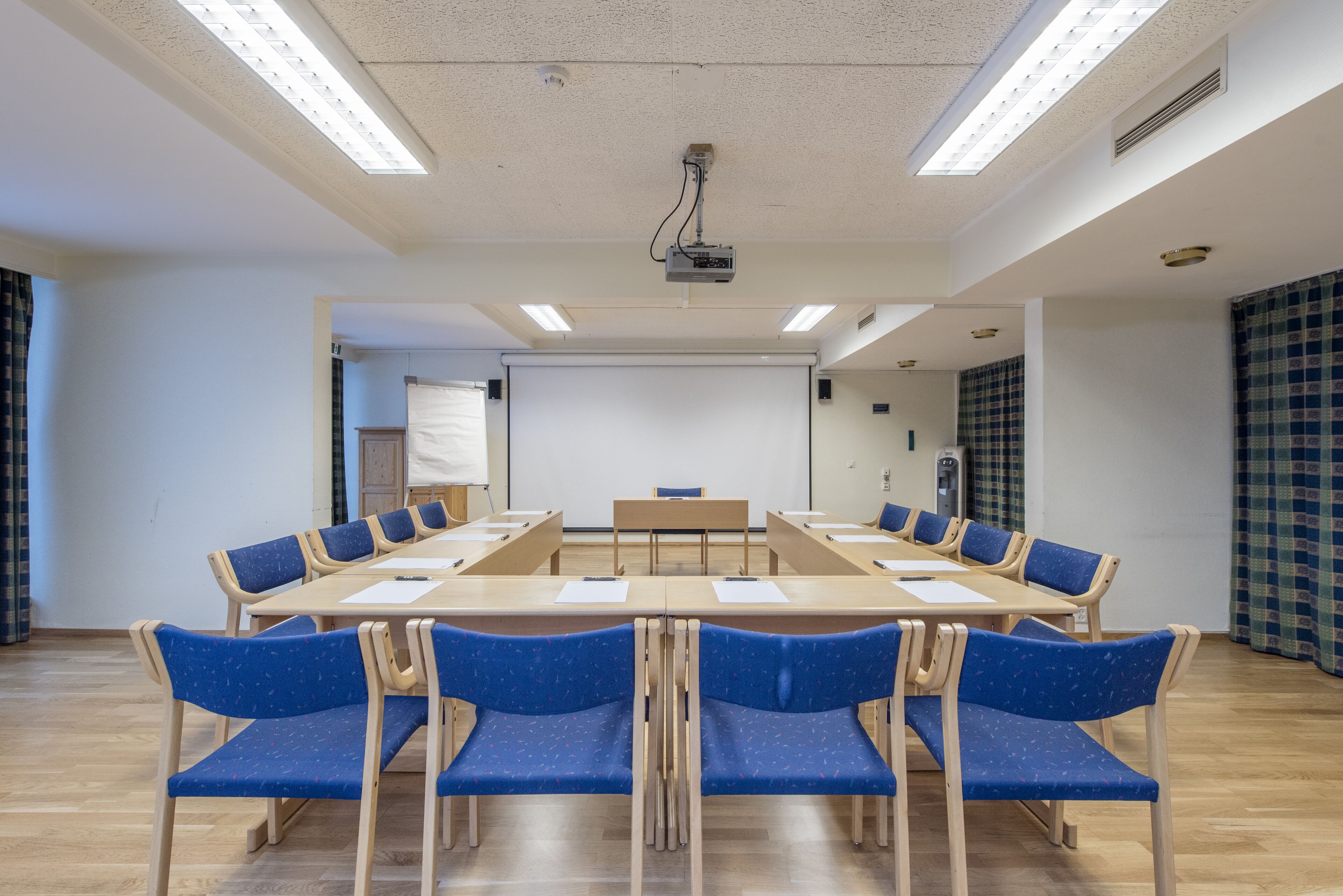 Un salón de conferencias con una larga mesa, sillas azules, un proyector y una pizarra.