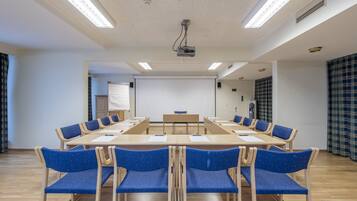 Un salón de conferencias con una larga mesa, sillas azules, un proyector y una pizarra.