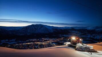 A snow-covered mountain at dusk with a town below and a helicopter on the right.