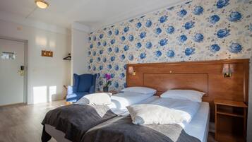 Ein Hotelzimmer mit zwei Betten, einem Holz-Kopfteil, floralem Wandpapier und einem blauen Stuhl.