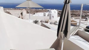 Un hombre en una bañera de hidromasaje con vista al mar y edificios blancos al fondo.