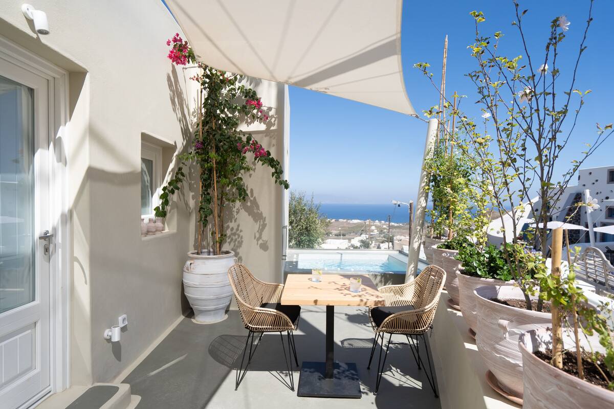 Un balcón con una mesa y sillas, plantas en macetas y vista al mar.