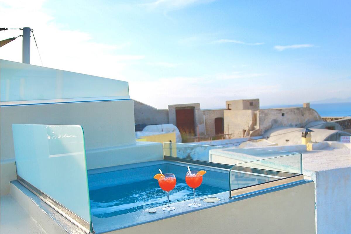Una piscina en la azotea con dos vasos de bebida roja, cielo despejado y edificios a lo lejos.