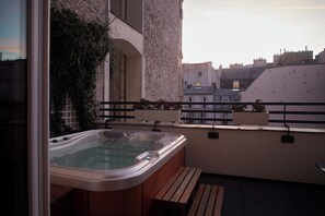 A balcony with a hot tub, wooden bench, and potted plants. - Paris j'Adore Hotel & Spa (Paris)