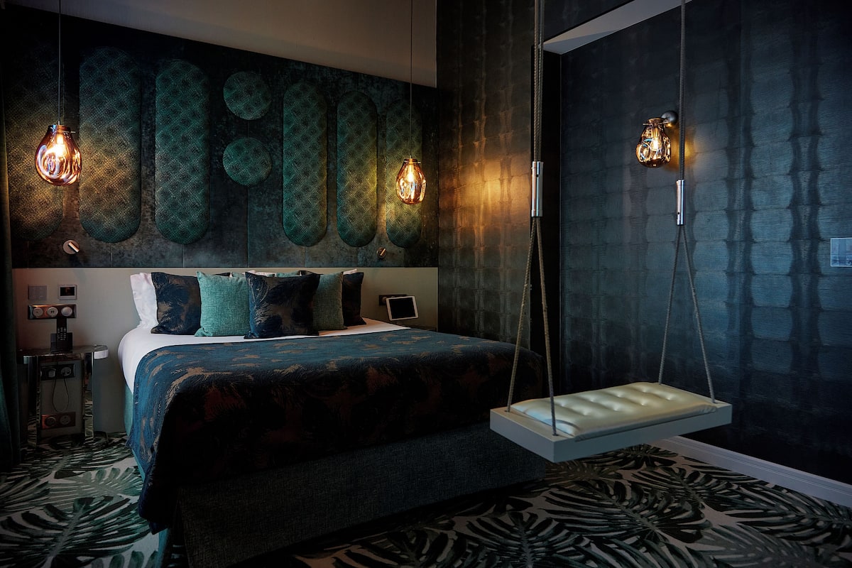 A modern bedroom with a large bed, a hanging swing, and wall-mounted lights.