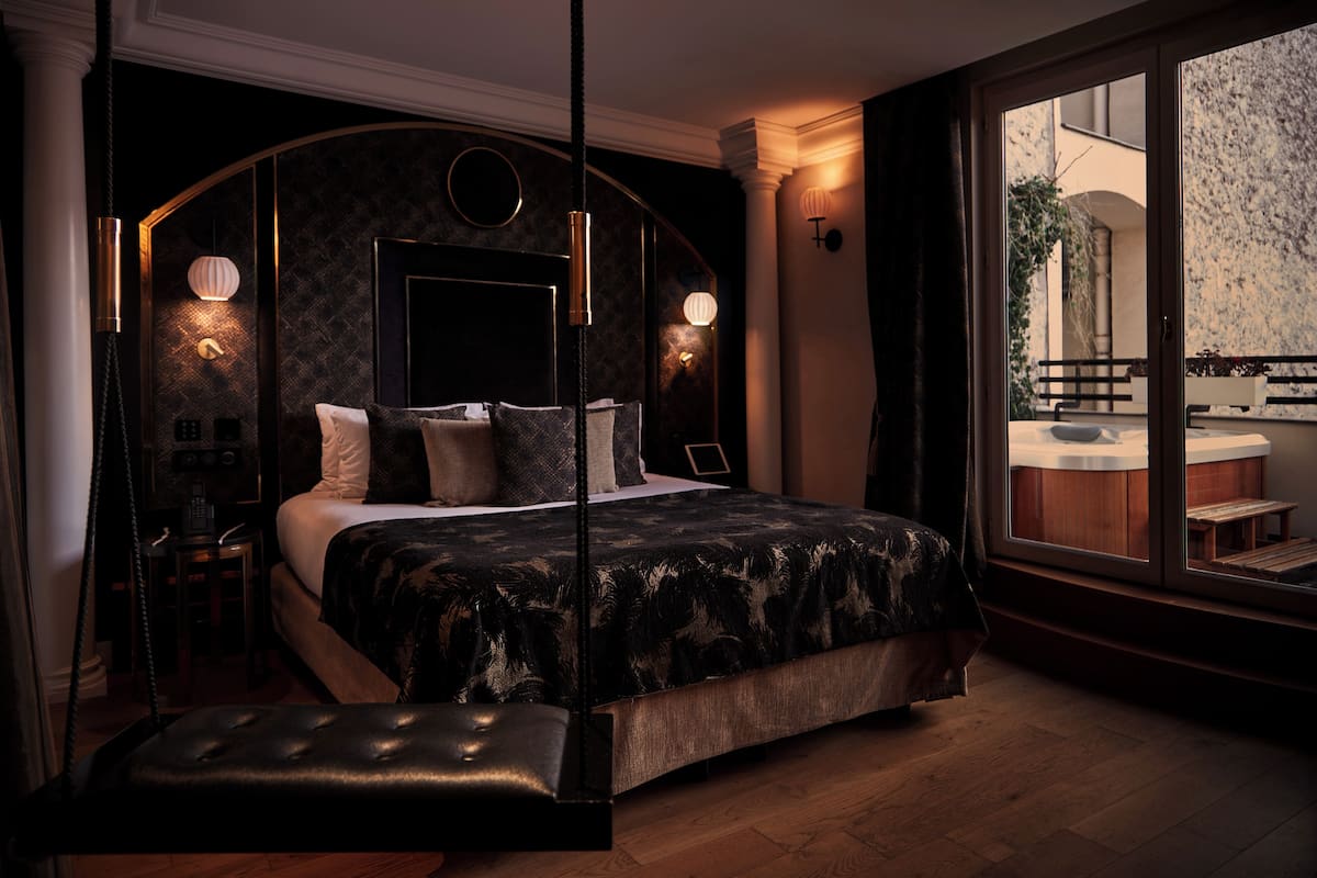 A modern bedroom with a large bed, a hanging chair, and a view of an outdoor balcony.