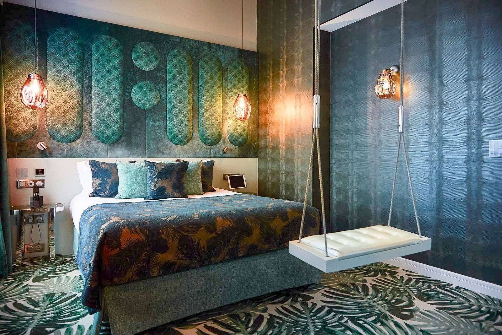 A modern bedroom with a bed, hanging lights, a swing chair, and a patterned wall.