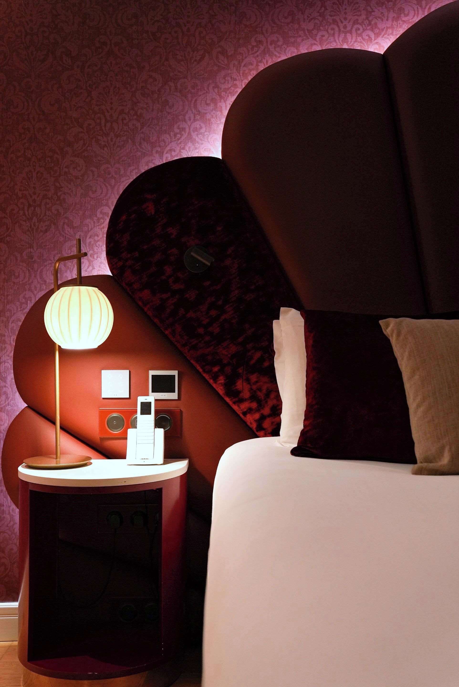 Een moderne slaapkamer met een gebogen hoofdeinde, een nachtkastje met een lamp en een wandpaneel.