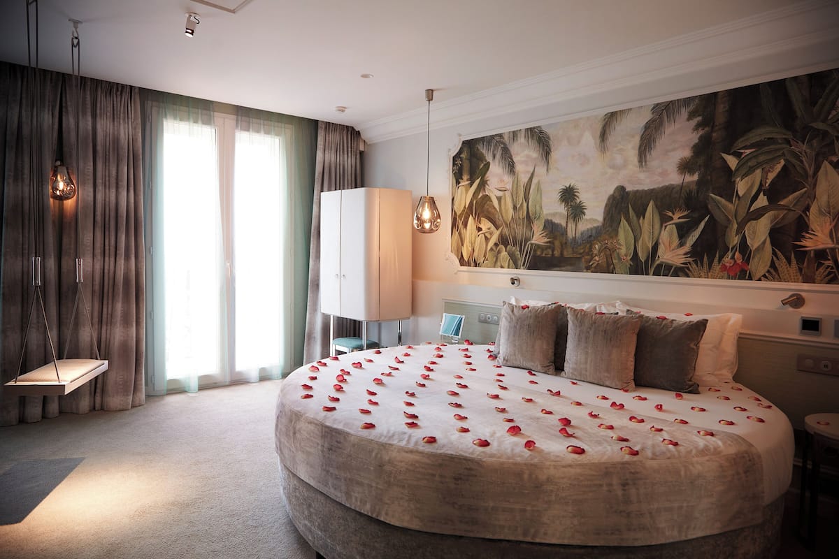A bedroom with a large bed, a nightstand, a desk, a hanging light, and a large painting on the wall.
