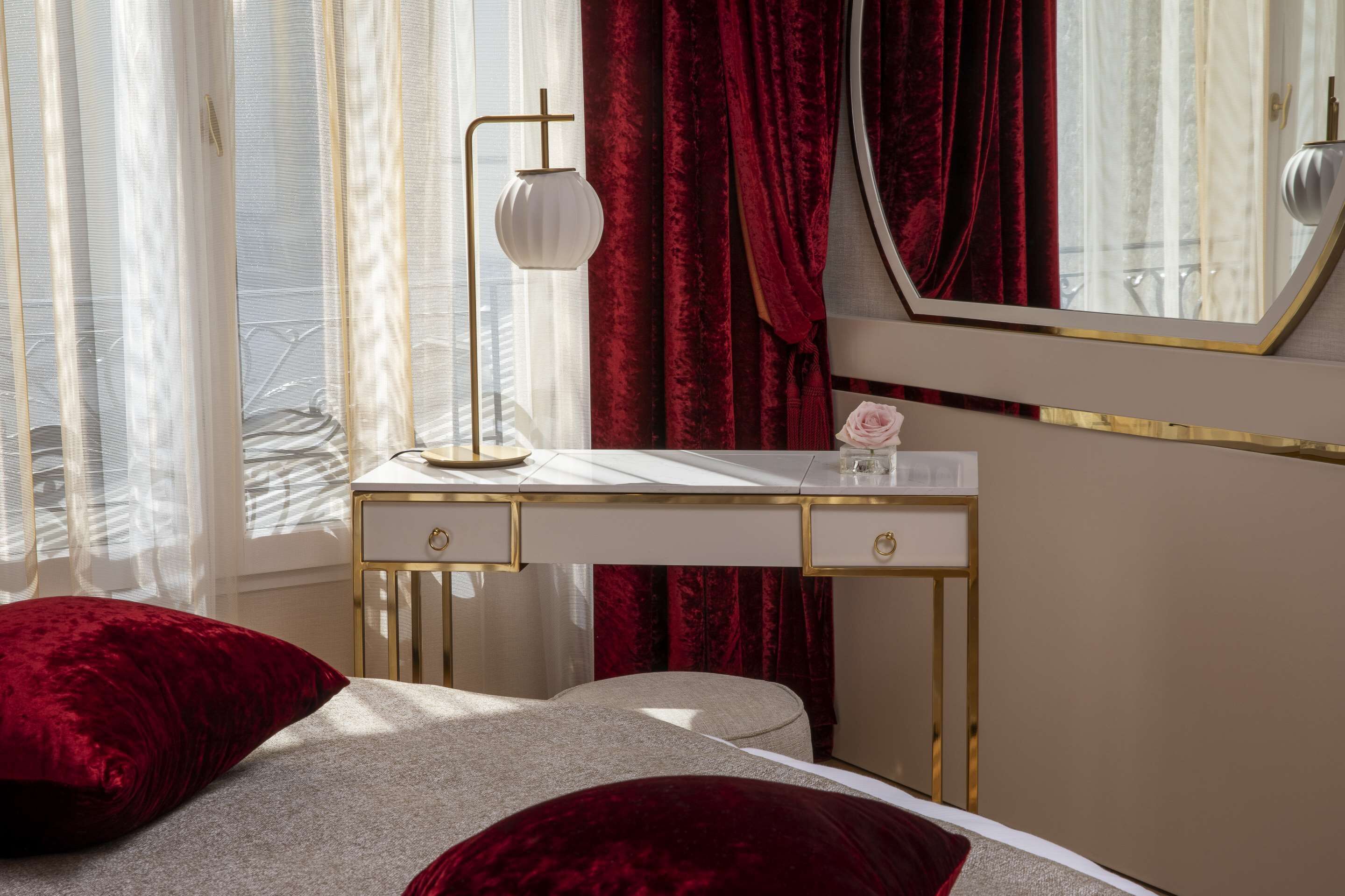 A bedroom with a bed, a bedside table, a mirror, and a window with curtains.