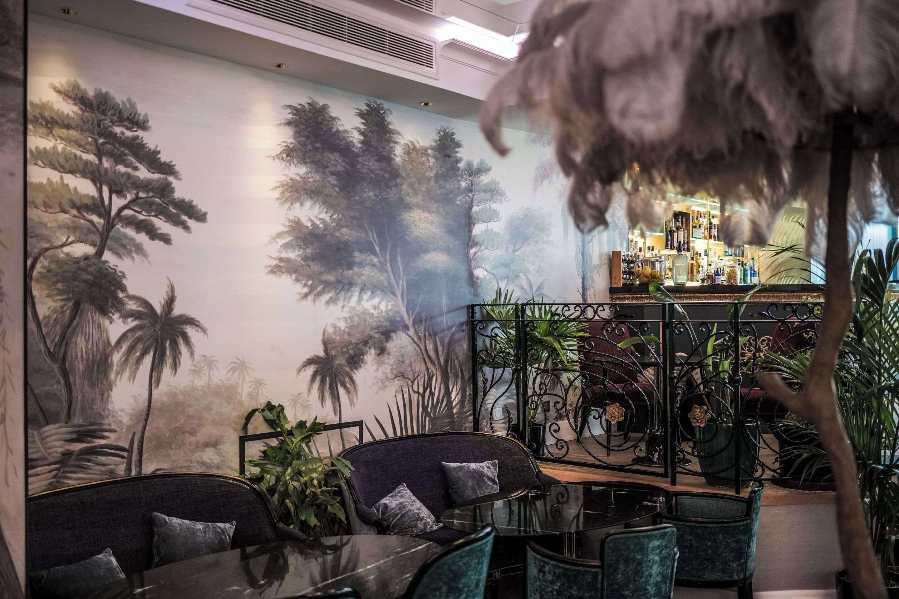 A bar area with a mural of trees and plants, seating with cushions, and a decorative feather.