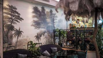 A bar area with a mural of trees and plants, seating with cushions, and a decorative feather.