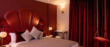 A modern hotel room with a large bed, a red headboard, a bedside table with a lamp, and a red curtain.