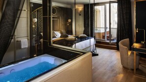 A modern hotel room with a large bathtub, a bed with multiple pillows, a sitting area with a chair, and a view of the city through large windows. - Paris j'Adore Hotel & Spa (Paris)