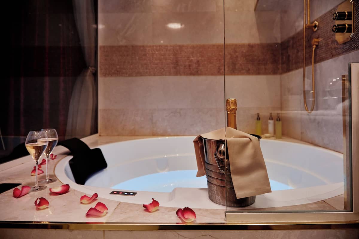 A luxurious bathroom with a bathtub, champagne, and rose petals.