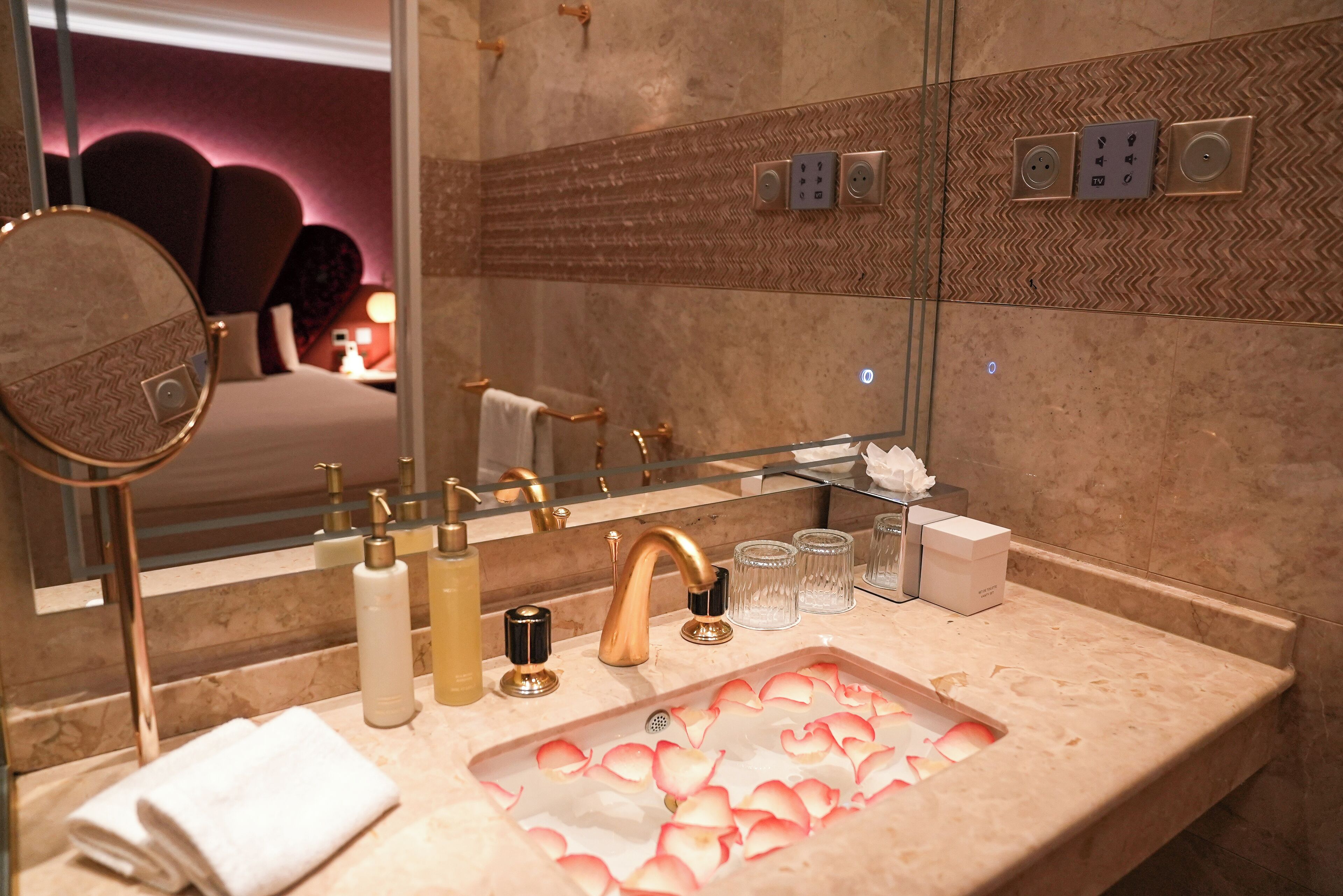 A bathroom with a marble sink, gold faucets, a mirror, and a towel.