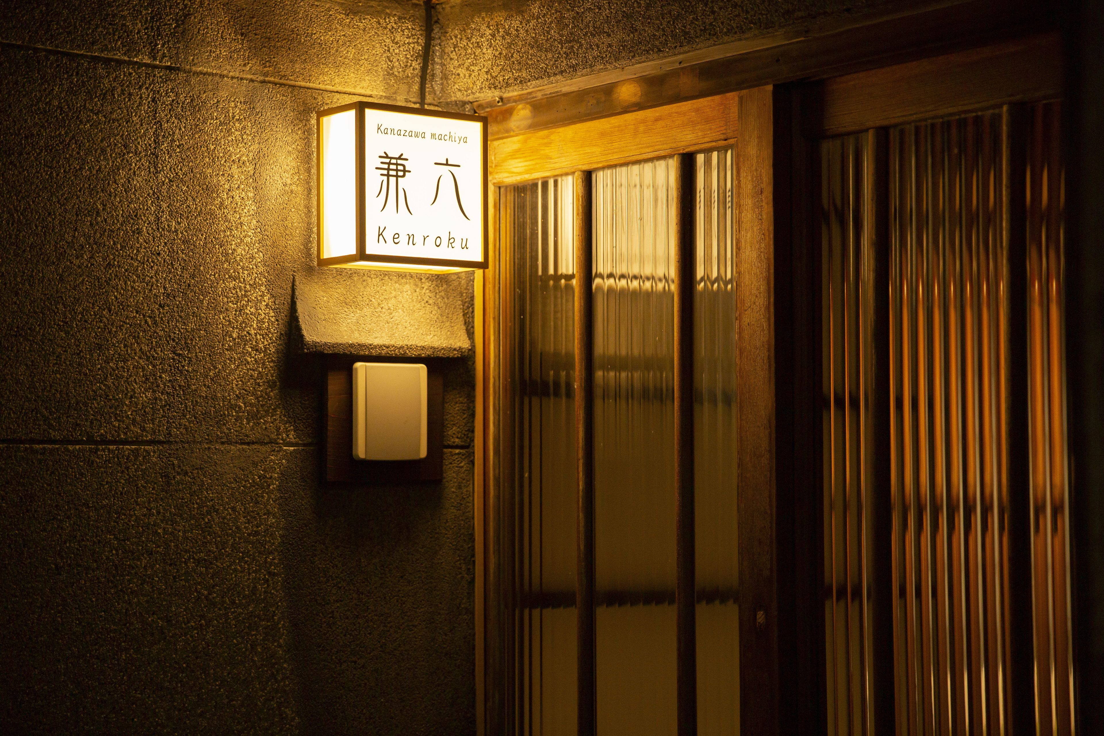 Entrada de um edifício tradicional japonês, com uma placa indicando o nome 'Kanazawa machiya Kenroku'.