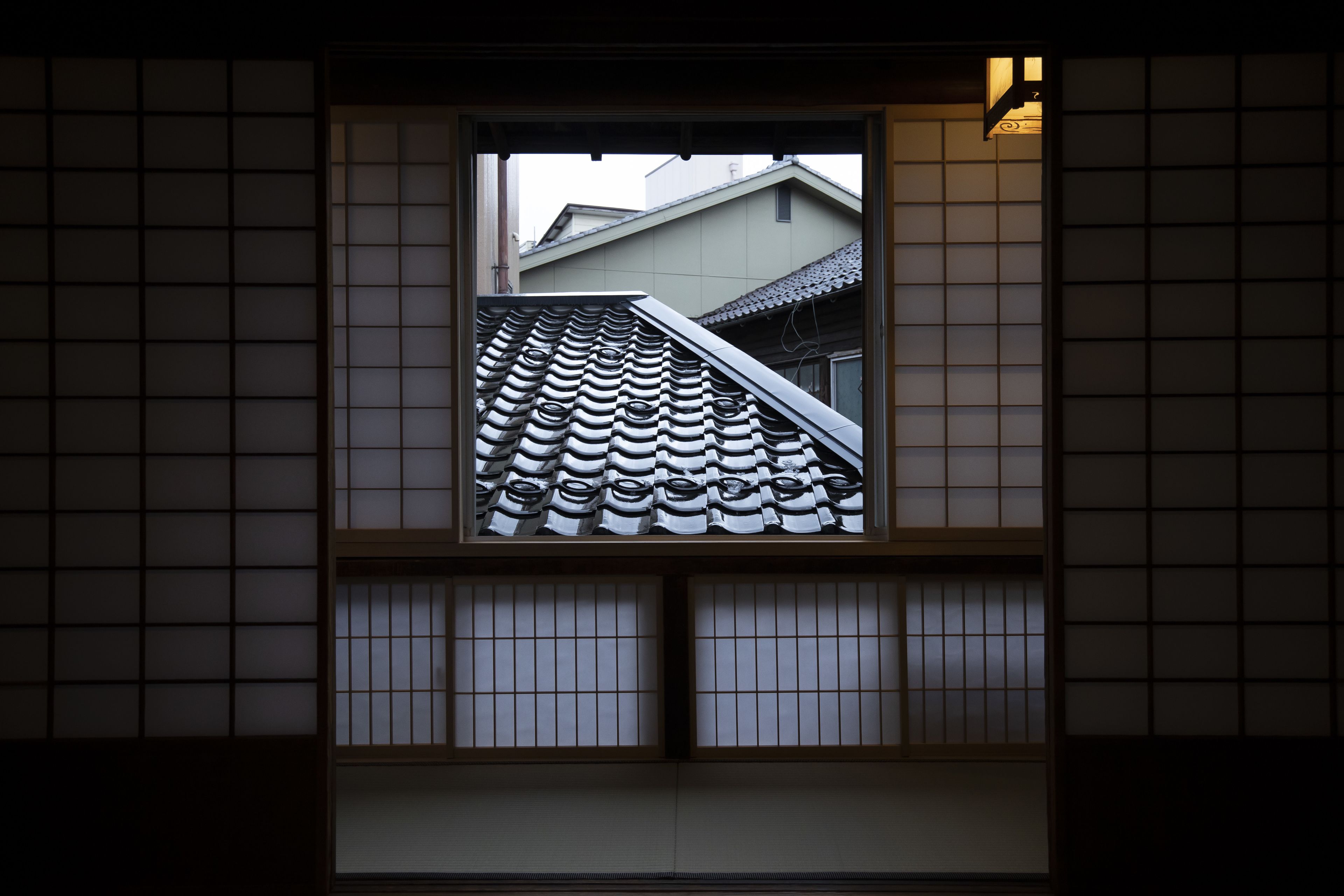 A traditional Japanese building with a tiled roof and a window framed by wooden lattice.