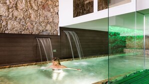 A person in a spa bath with two waterfalls, a stone wall, and a glass enclosure. - Re Dionisio Luxury Suites (Syracuse)