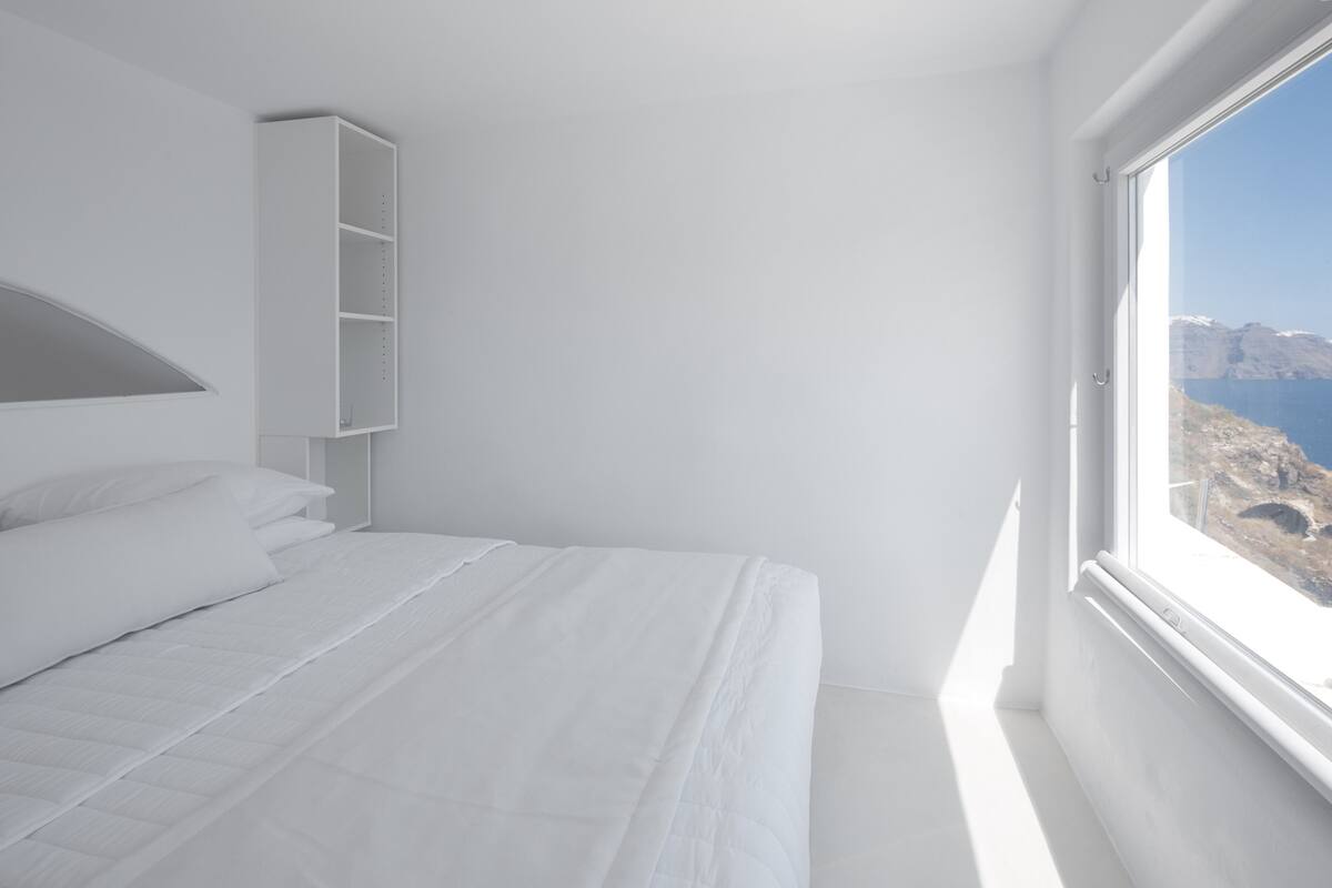 Quarto minimalista com uma grande janela, uma cama e uma estante embutida.