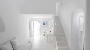 A modern, minimalist interior with a staircase, a dining area, and a living space. - Oia White Cave Oia Cliff (Santorini)