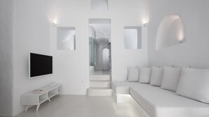 A modern, minimalist living room with a flat-screen TV, a white sofa, and a staircase leading to another level. - Oia White Cave Oia Cliff (Santorini)