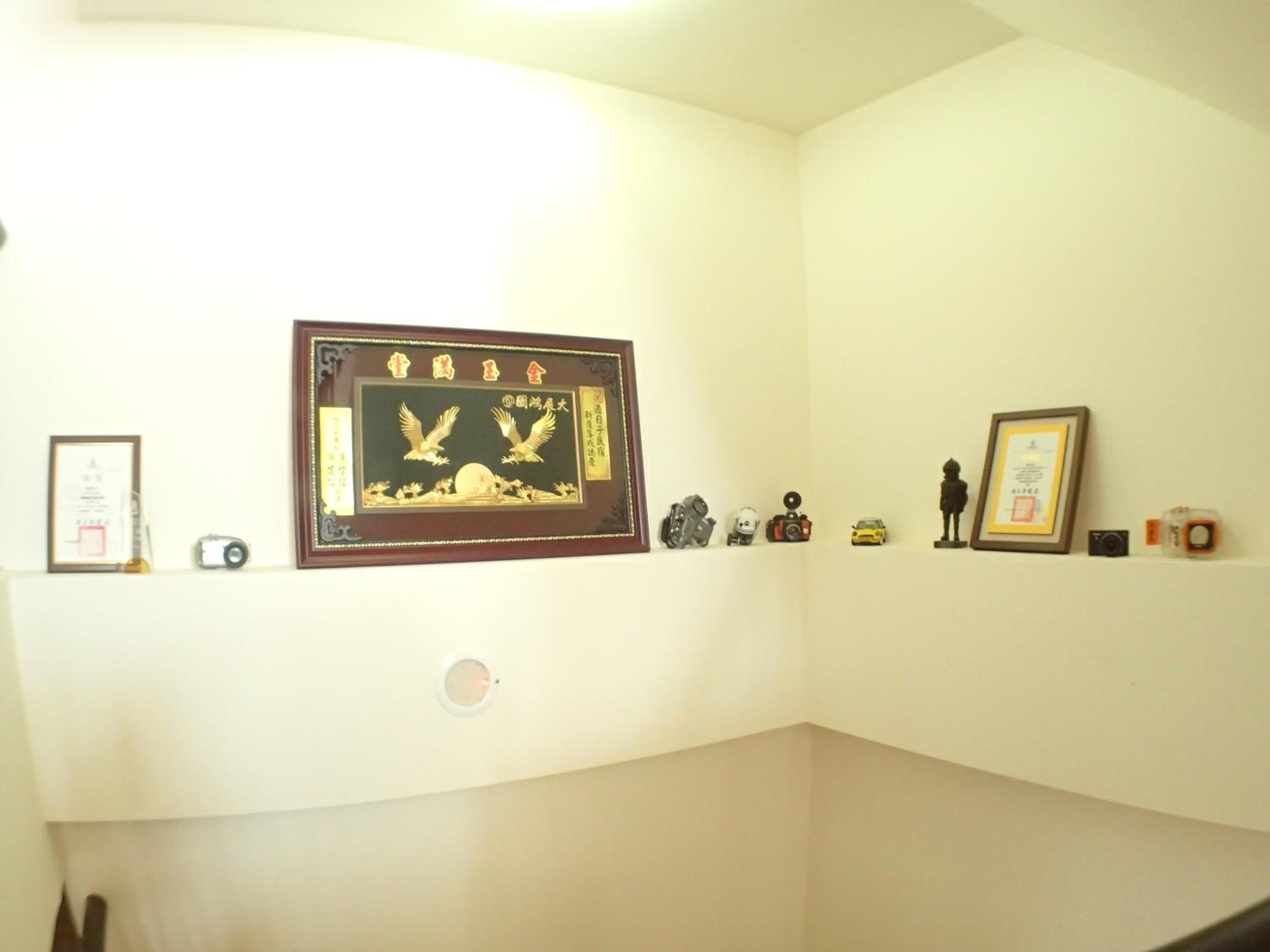 Une pièce dans laquelle on trouve une étagère fixée au mur, sur laquelle sont exposés divers objets, notamment des œuvres d’art encadrées, un appareil photo et de petites figurines.