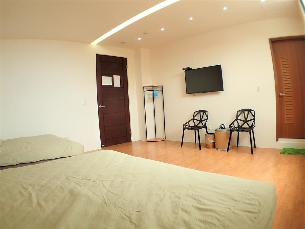 Un dormitorio con cama, televisor montado en la pared y dos sillones.