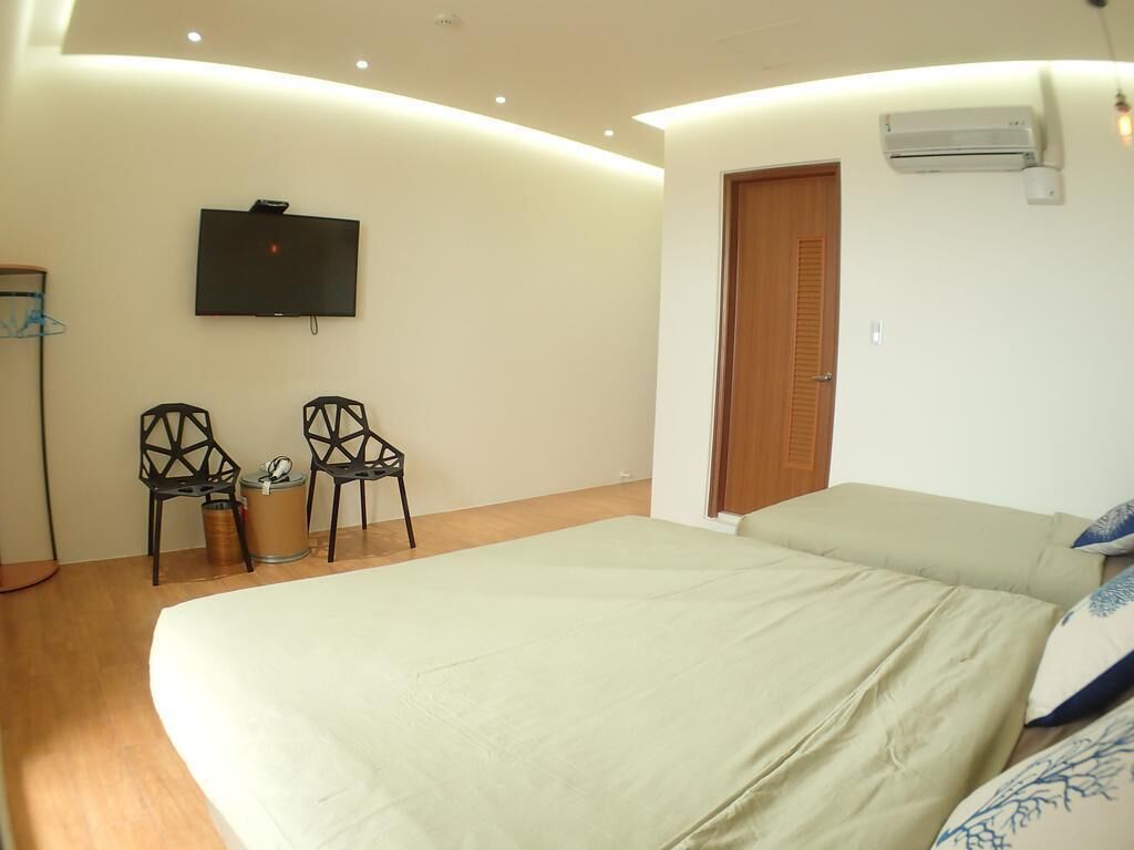 A bedroom with a bed, two chairs, a television, and a door.