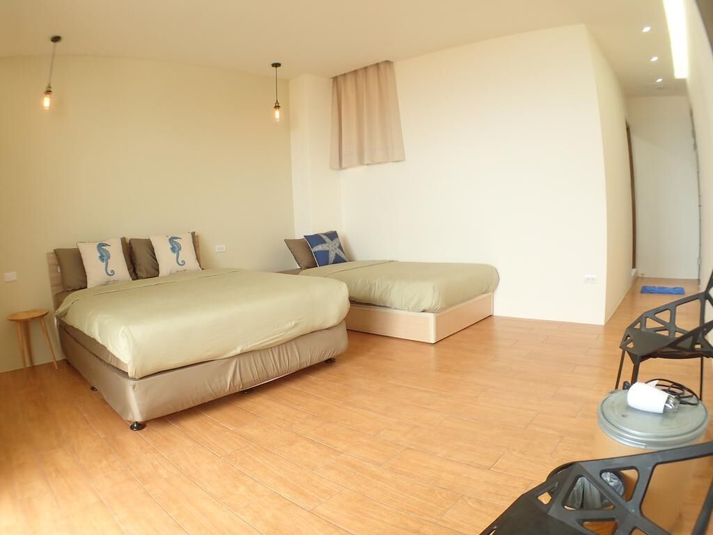 A bedroom with a large bed, a smaller bed, a chair, and a table with a lamp.