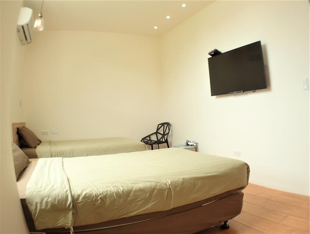 Une chambre avec deux lits, un téléviseur à écran plat fixé au mur, une chaise et une petite table.