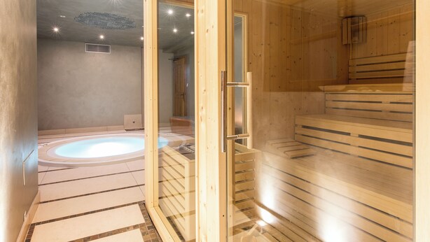 Uma sala de sauna com porta de vidro, um banco de madeira e uma banheira de hidromassagem.