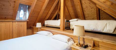 A wooden attic bedroom with two beds, a nightstand with a lamp, and a window with curtains.