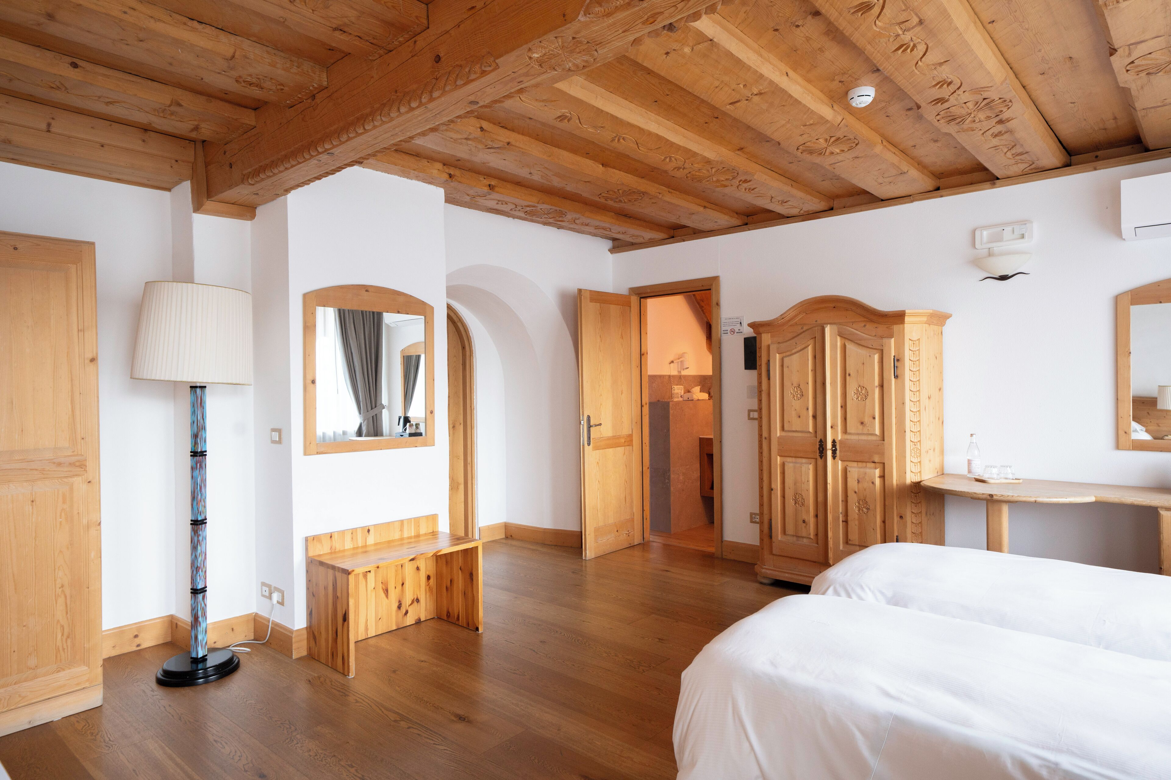 A room with wooden floors, a bed, a desk, a mirror, and a wardrobe.