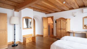 A room with wooden floors, a bed, a desk, a mirror, and a wardrobe.
