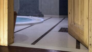 Entrada de um spa com porta de madeira, piso ladrilhado e placa indicando "HE SPA".