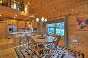 A wooden cabin with a dining area, kitchen, and large windows.