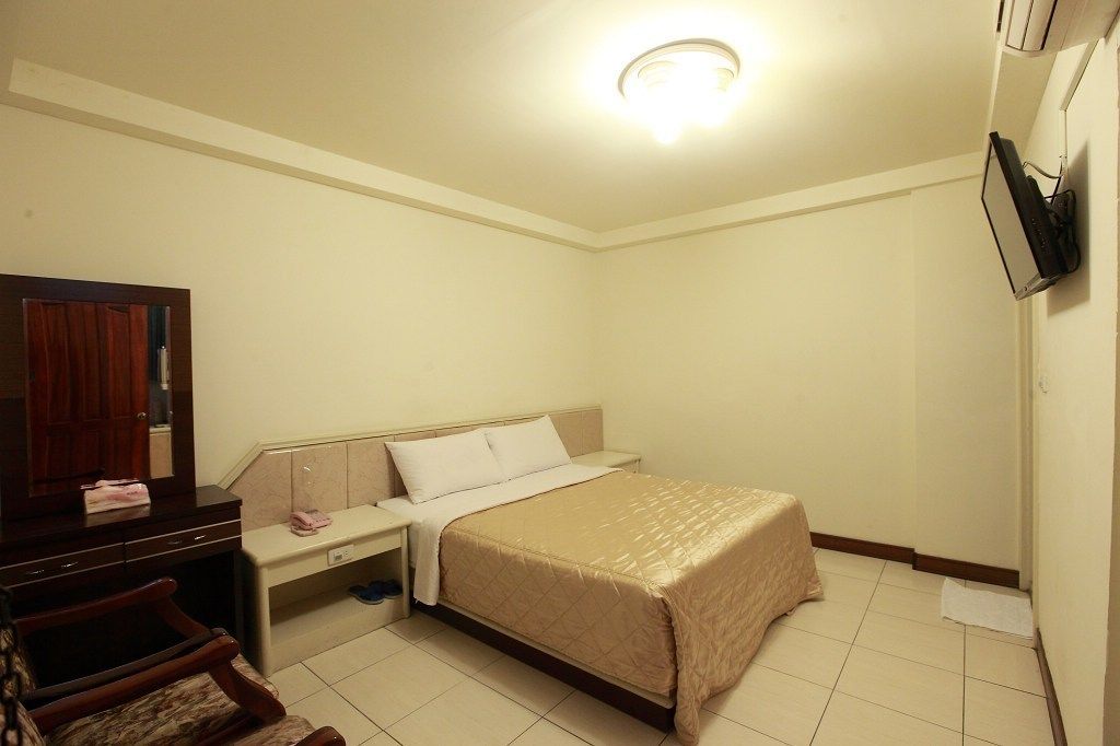 Une chambre à coucher avec un lit, une table de chevet, une commode, une chaise et un téléviseur fixé au mur.