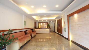 A hotel lobby with a reception desk, seating area, and a plant.