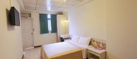 Habitación de hotel con una cama grande, una mesita de noche con teléfono, un espejo y una ventana con cortinas.