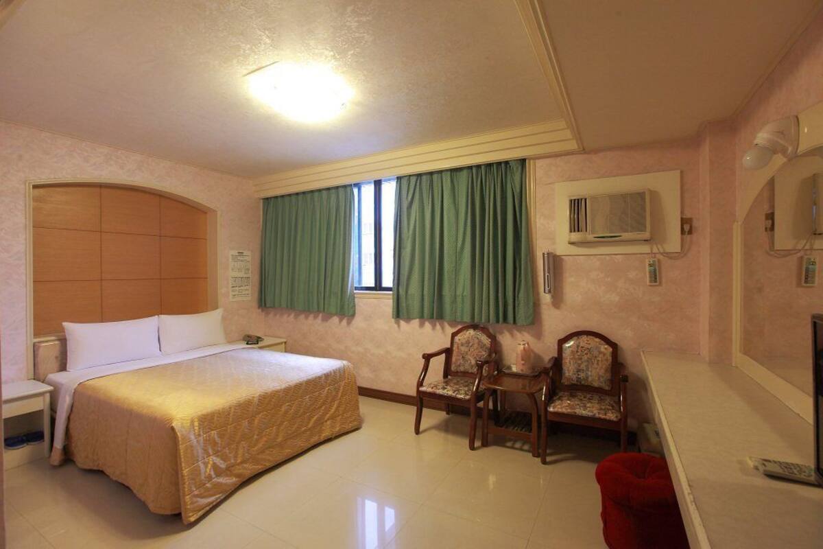 Une chambre d’hôtel avec un grand lit, deux fauteuils, un bureau et un téléviseur.