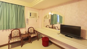 A room with a television, two chairs, a small table, a mirror, and a red ottoman.