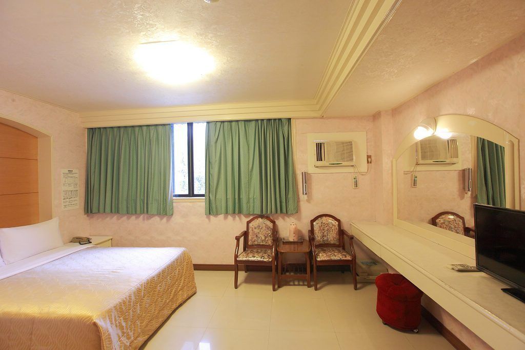 Habitación de hotel con cama, dos sillas, televisión y espejo.