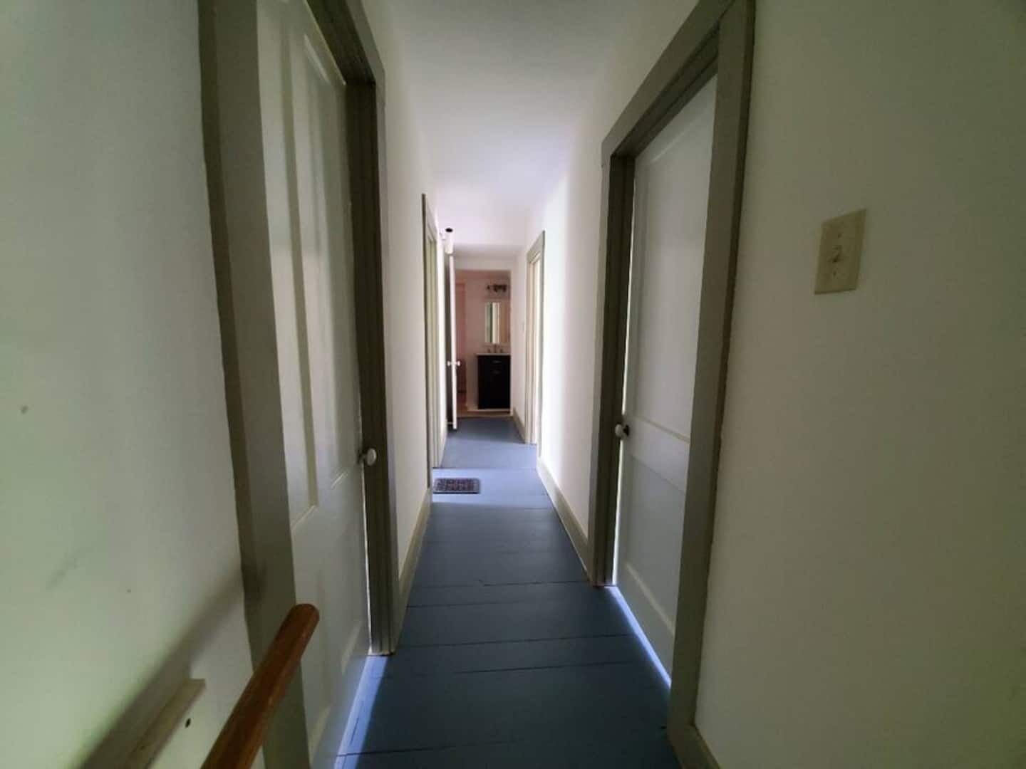 Un pasillo estrecho con alfombra azul, paredes blancas y puertas de madera.