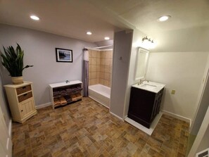 A bathroom with a bathtub, a sink, and a shower. There is a plant on a shelf and a framed picture on the wall. - Classic Vermont Farmhouse near Sugarbush Resort (Warren)