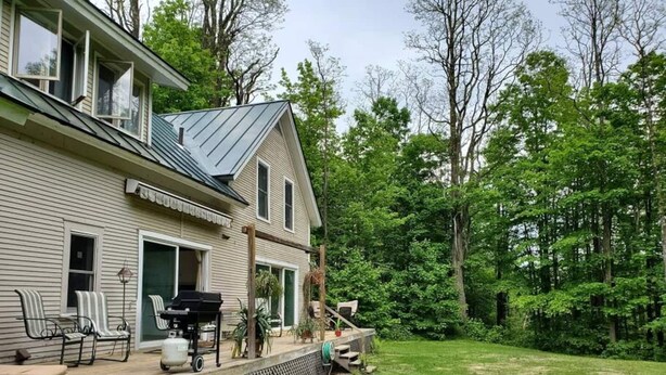 A two-story house with a covered porch, outdoor seating, and a lawn.