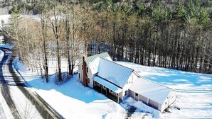 A rural property with a large barn and a house with a metal roof, surrounded by trees and a snowy landscape.